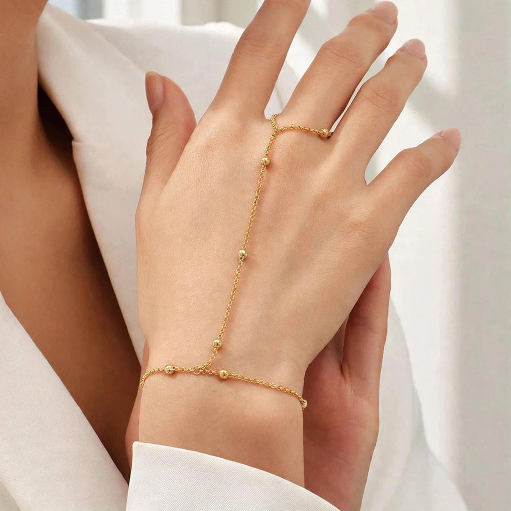 A delicate gold chain hand bracelet with matching ring and bracelet set on a model's hand, styled with a white blazer.