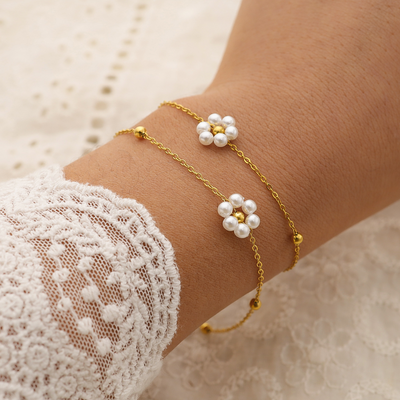 Gold bracelet with pearl flower charms on a wrist wearing a lace sleeve.
