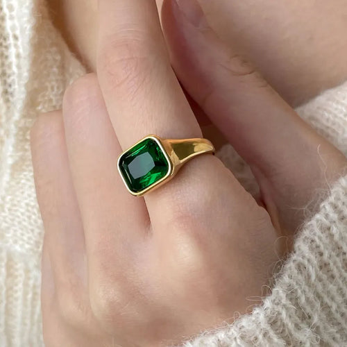 Gold ring with a green gemstone on a hand against a neutral background