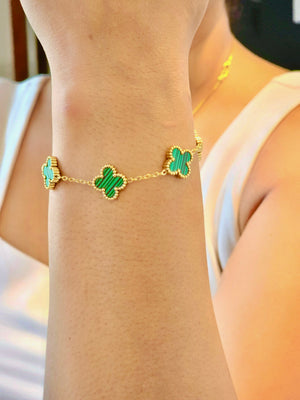 Gold bracelet with green clover-shaped charms on a wrist.