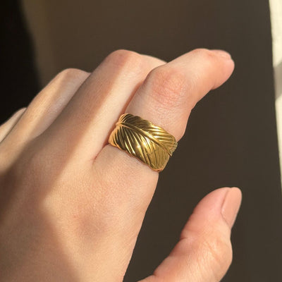 Gold leaf ring on a person's finger with a dark background