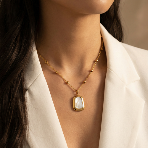 Gold necklace with a pendant worn by a person in a white blazer.