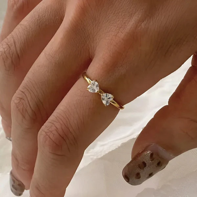 Close-up of a hand wearing a gold ring with heart-shaped diamonds on a neutral background