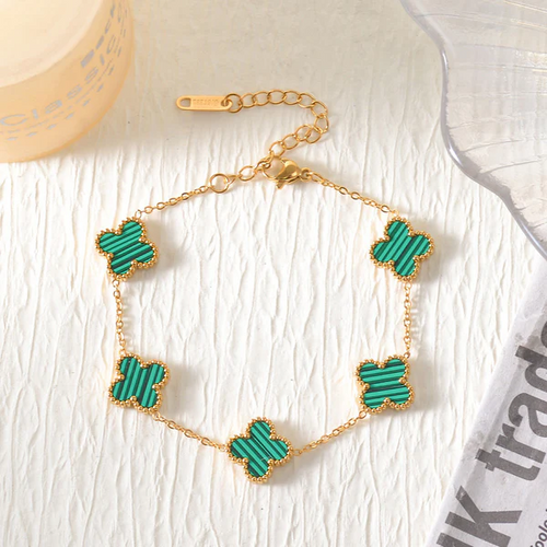 Gold bracelet with green clover-shaped charms on a light wooden surface.